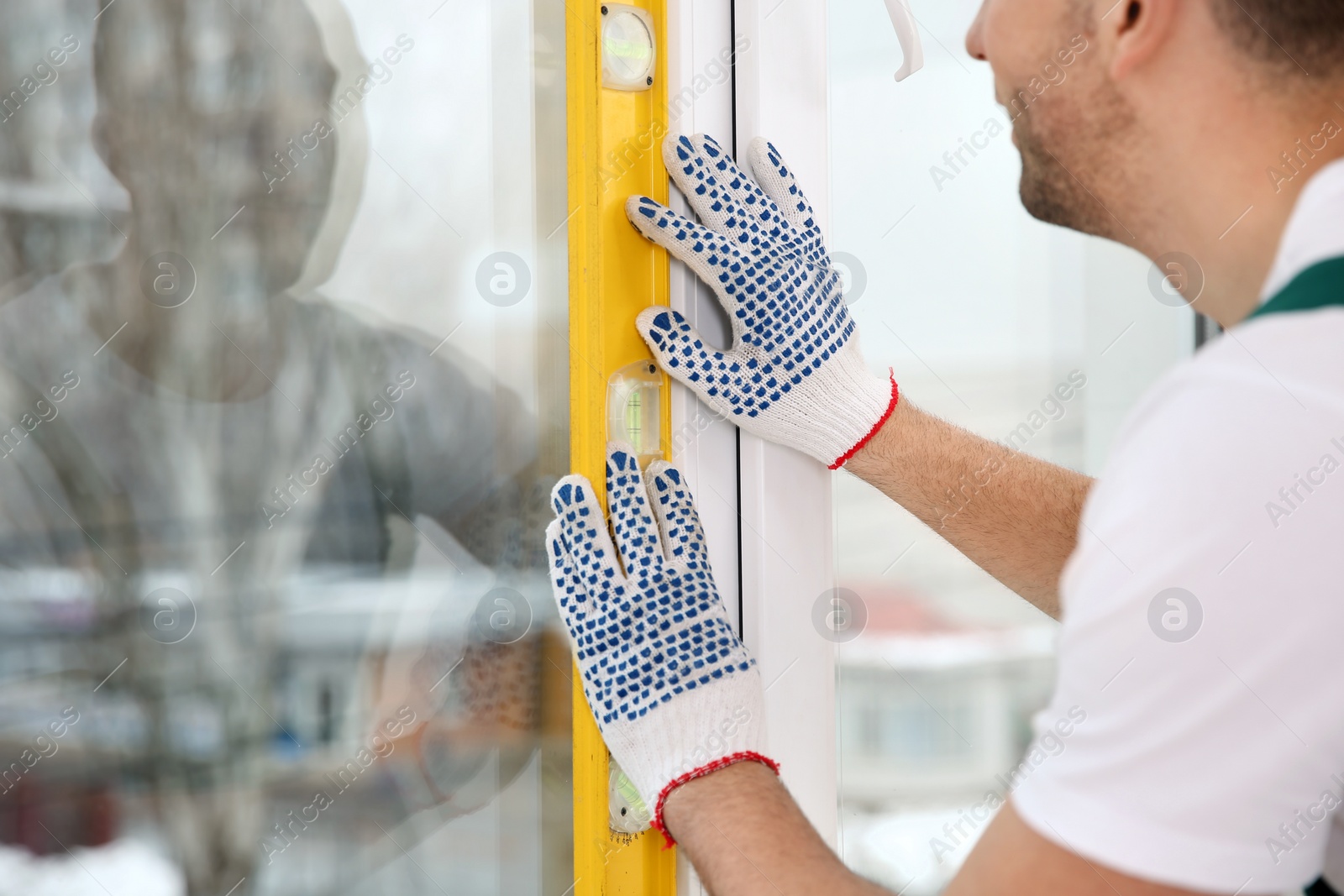 Photo of Construction worker using bubble level while installing window indoors, closeup