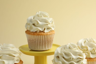 Photo of Tasty vanilla cupcakes with cream on pale yellow background, closeup