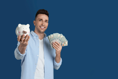 Photo of Happy man with cash money and piggybank against blue background, focus on hand. Space for text