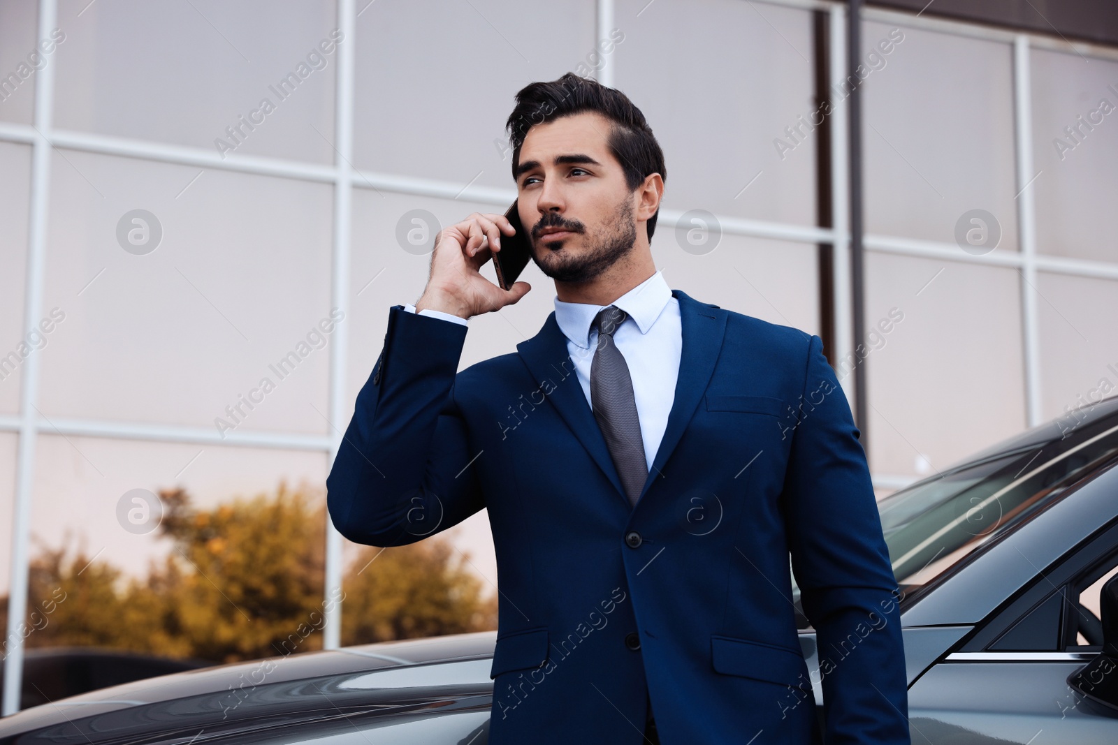 Photo of Attractive young man talking on phone near luxury car outdoors