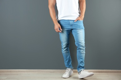 Photo of Young man in stylish jeans near grey wall with space for text, focus on legs