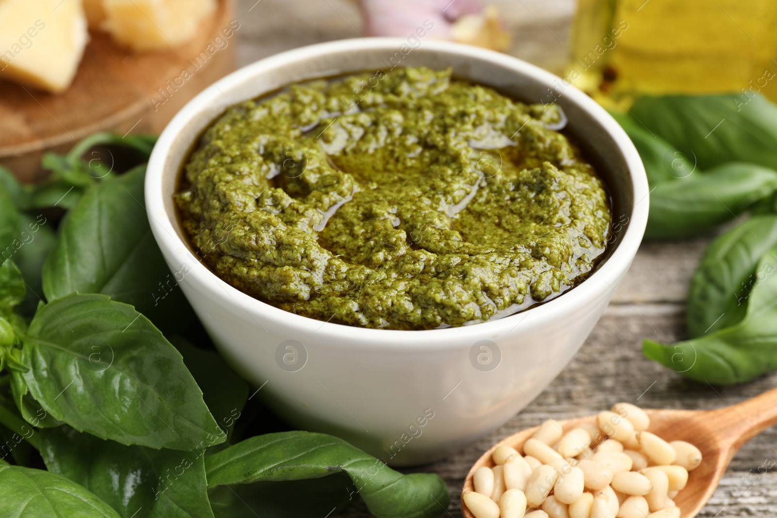 Photo of Tasty pesto sauce in bowl, pine nuts and basil on wooden table, closeup