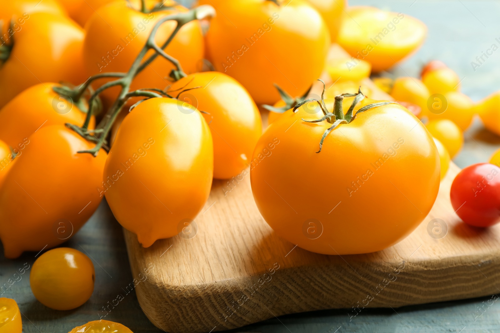 Photo of Ripe yellow tomatoes on light blue wooden table, closeup