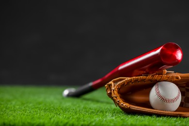 Baseball bat, leather glove and ball on green grass against dark background. Space for text