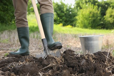 Photo of Worker digging soil with shovel outdoors, closeup
