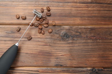 Black milk frother wand and coffee beans on wooden table, top view. Space for text