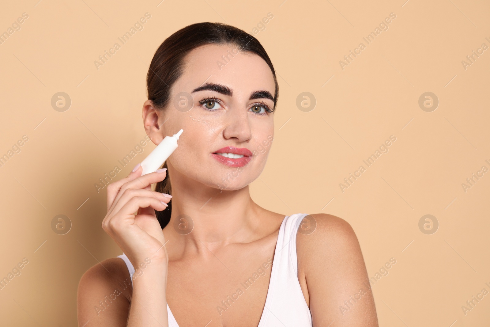 Photo of Woman with cosmetic product around eye on beige background. Space for text