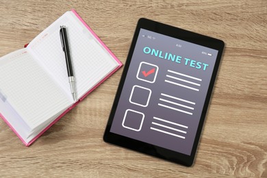 Modern tablet with online test, notebook and pen on wooden table, flat lay