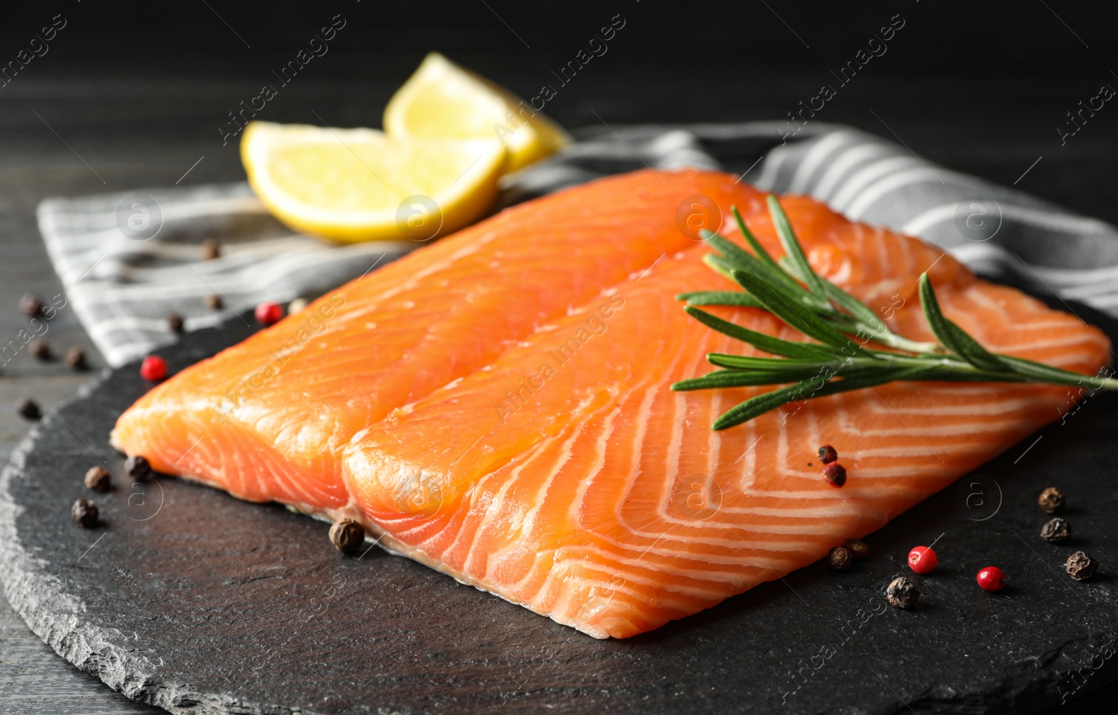 Photo of Fresh salmon fillet with rosemary on slate board, closeup