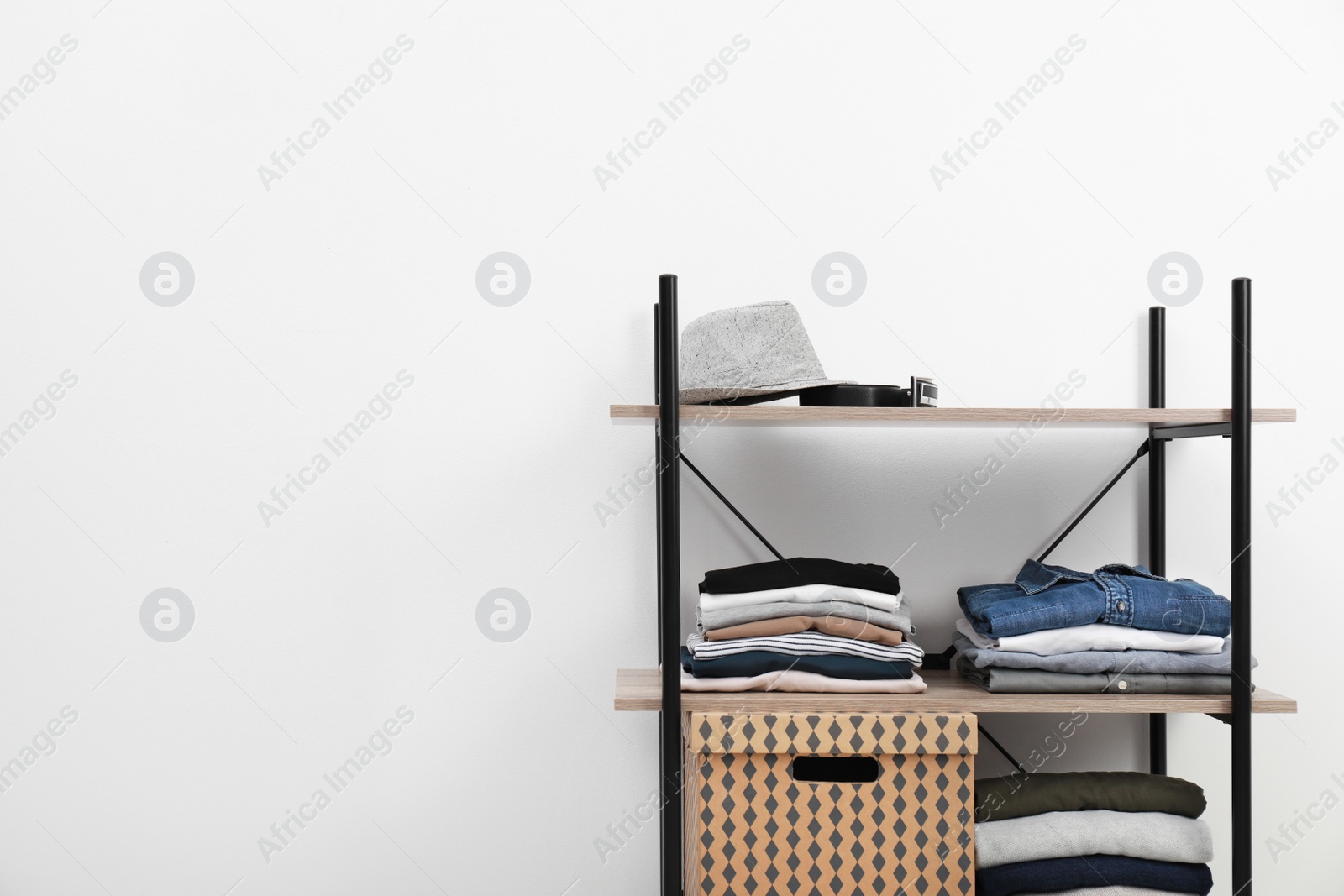 Photo of Shelves unit with stacked clothes and box near white wall. Space for text