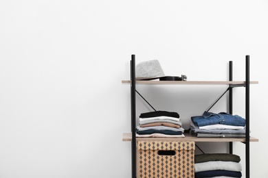 Photo of Shelves unit with stacked clothes and box near white wall. Space for text