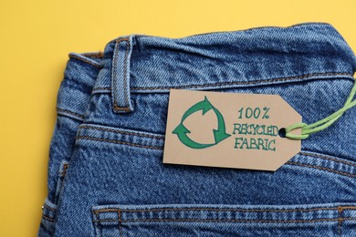 Photo of Jeans with recycling label on yellow background, closeup