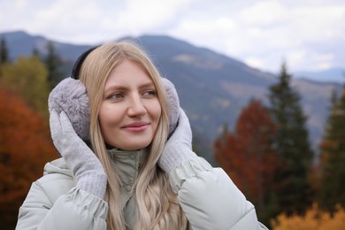 Photo of Young beautiful woman wearing warm earmuffs in mountains