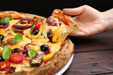 Photo of Woman taking slice of tasty vegetable pizza at wooden table, closeup