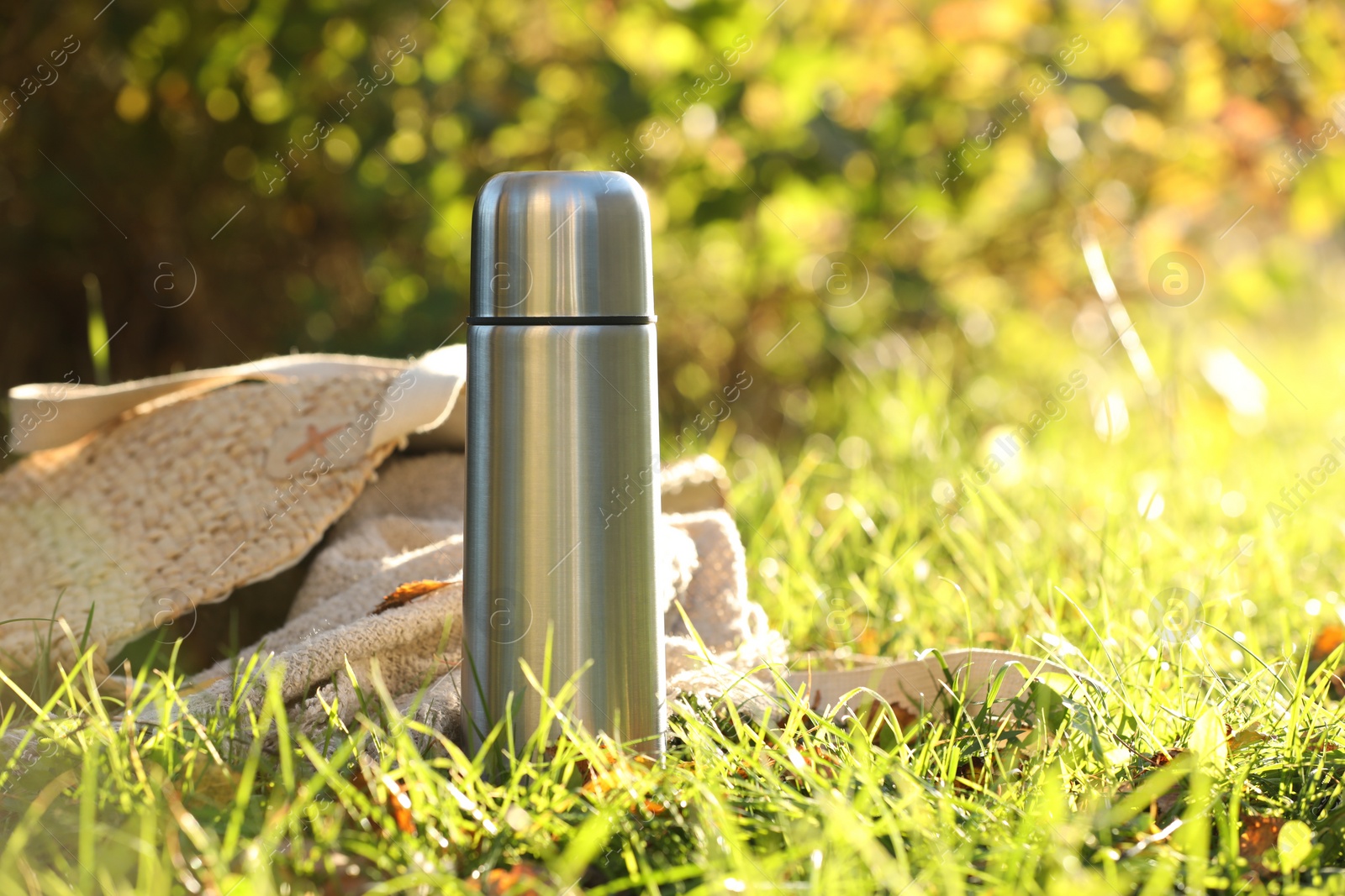 Photo of Metal thermos and bag with blanket on green grass outdoors, space for text