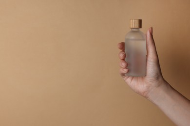 Woman holding bottle of cosmetic product on beige background, closeup. Space for text