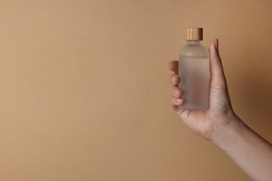 Photo of Woman holding bottle of cosmetic product on beige background, closeup. Space for text