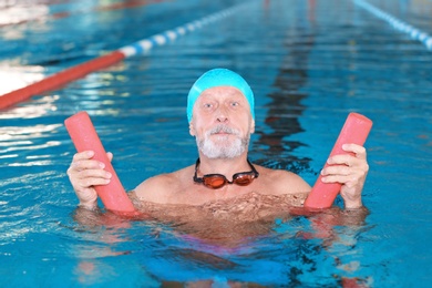 Photo of Sportive senior man with swimming noodle in indoor pool