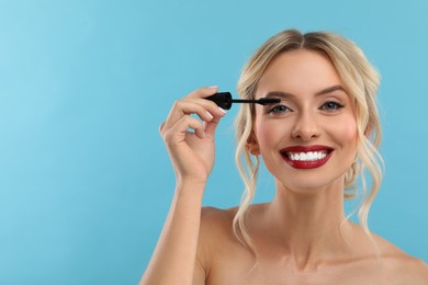 Photo of Beautiful makeup. Smiling woman applying mascara on light blue background, space for text