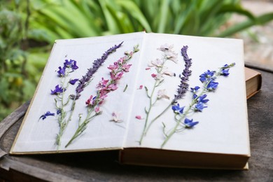 Photo of Book with beautiful dried flowers on wooden table outdoors, closeup