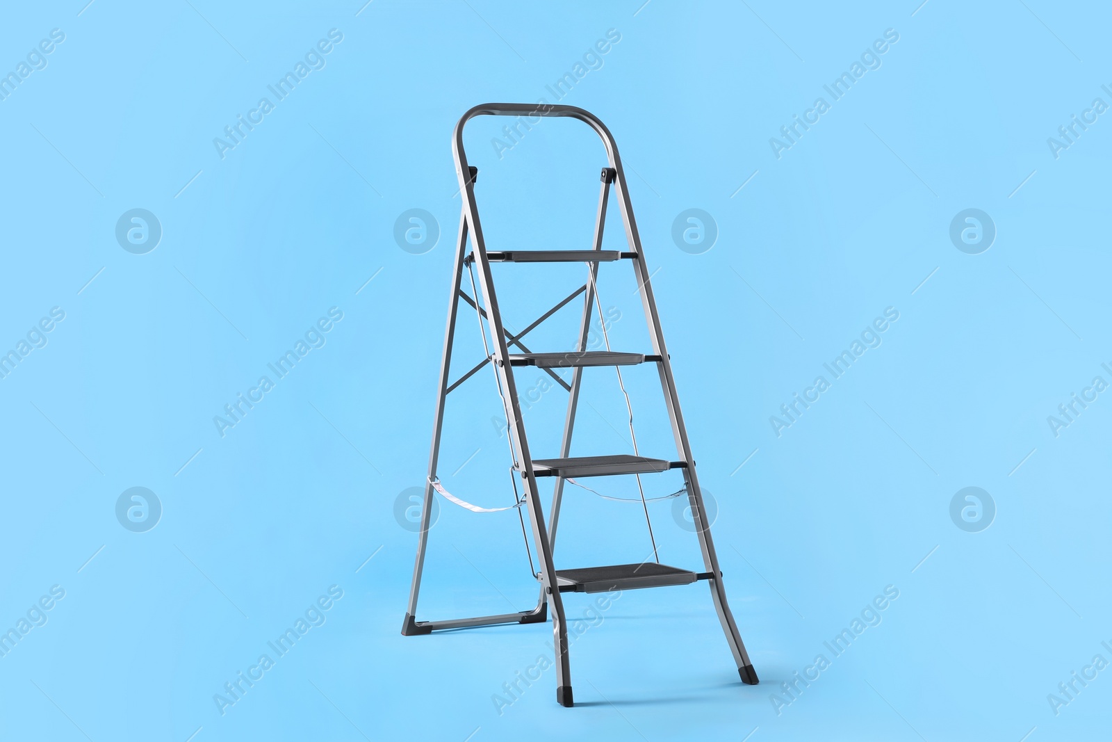 Photo of Metal stepladder on light blue background. Construction equipment