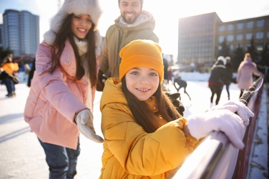 Photo of Cute little girl with her parents at outdoor ice skating rink