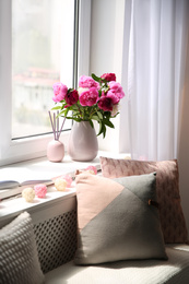 Photo of Comfortable place for rest with cushions and peony flowers near window indoors