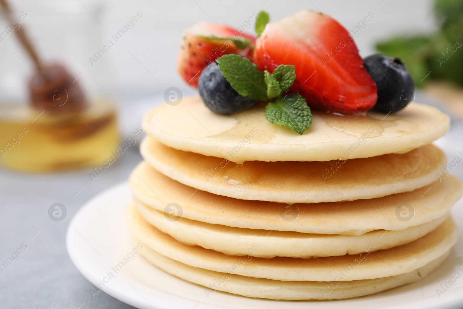 Photo of Stack of tasty pancakes with fresh berries, mint and honey on light grey table, closeup