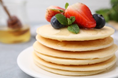 Stack of tasty pancakes with fresh berries, mint and honey on light grey table, closeup