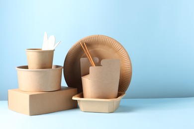 Photo of Eco friendly food packaging. Paper containers and tableware on white table against light blue background, space for text