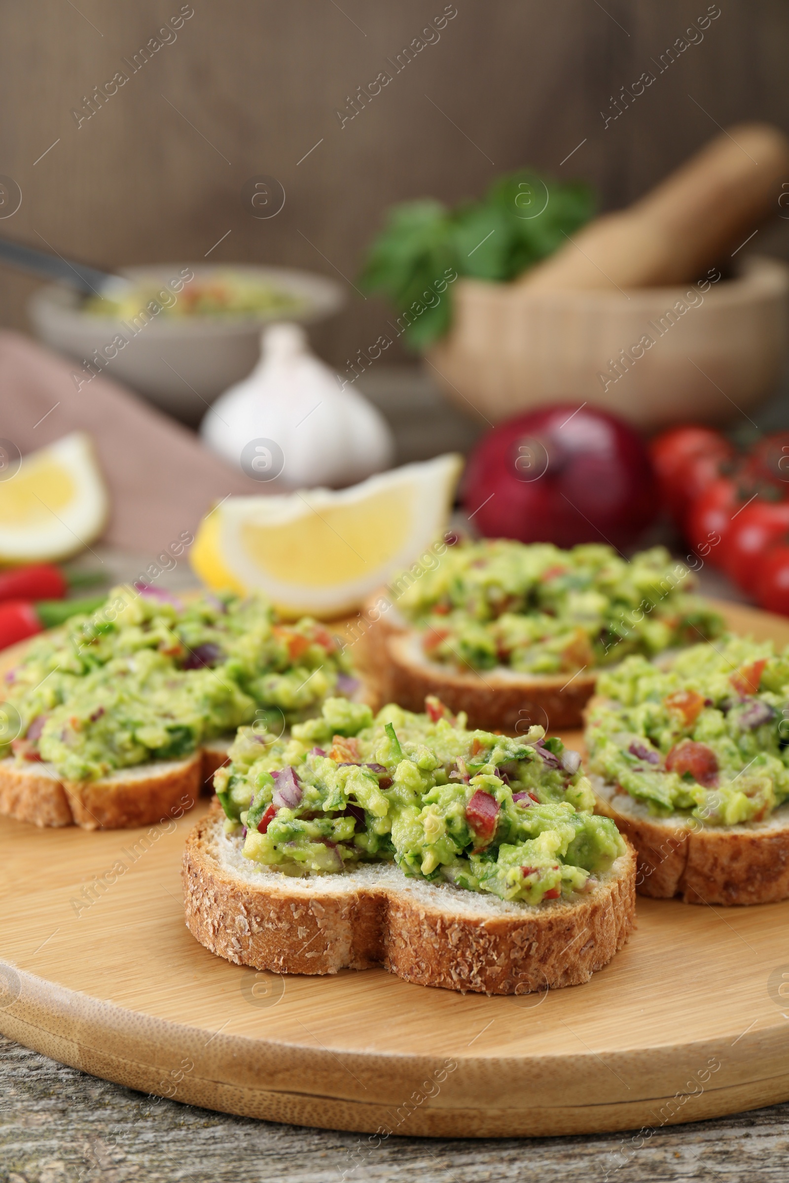 Photo of Slices of bread with tasty guacamole and ingredients on wooden table, closeup