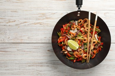 Photo of Shrimp stir fry with vegetables in wok and chopsticks on light wooden table, top view. Space for text