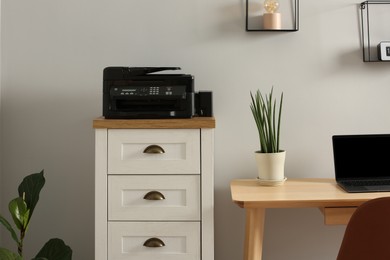 Photo of Modern printer on chest of drawers near wooden table indoors