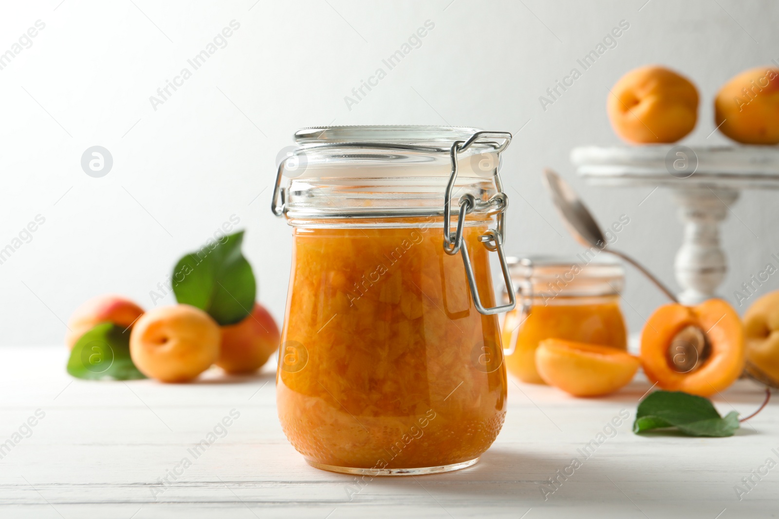 Photo of Jar of apricot jam and fresh fruits on white wooden table