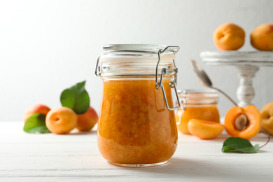 Jar of apricot jam and fresh fruits on white wooden table