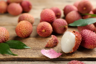 Photo of Fresh ripe lychees with leaves on wooden table, closeup