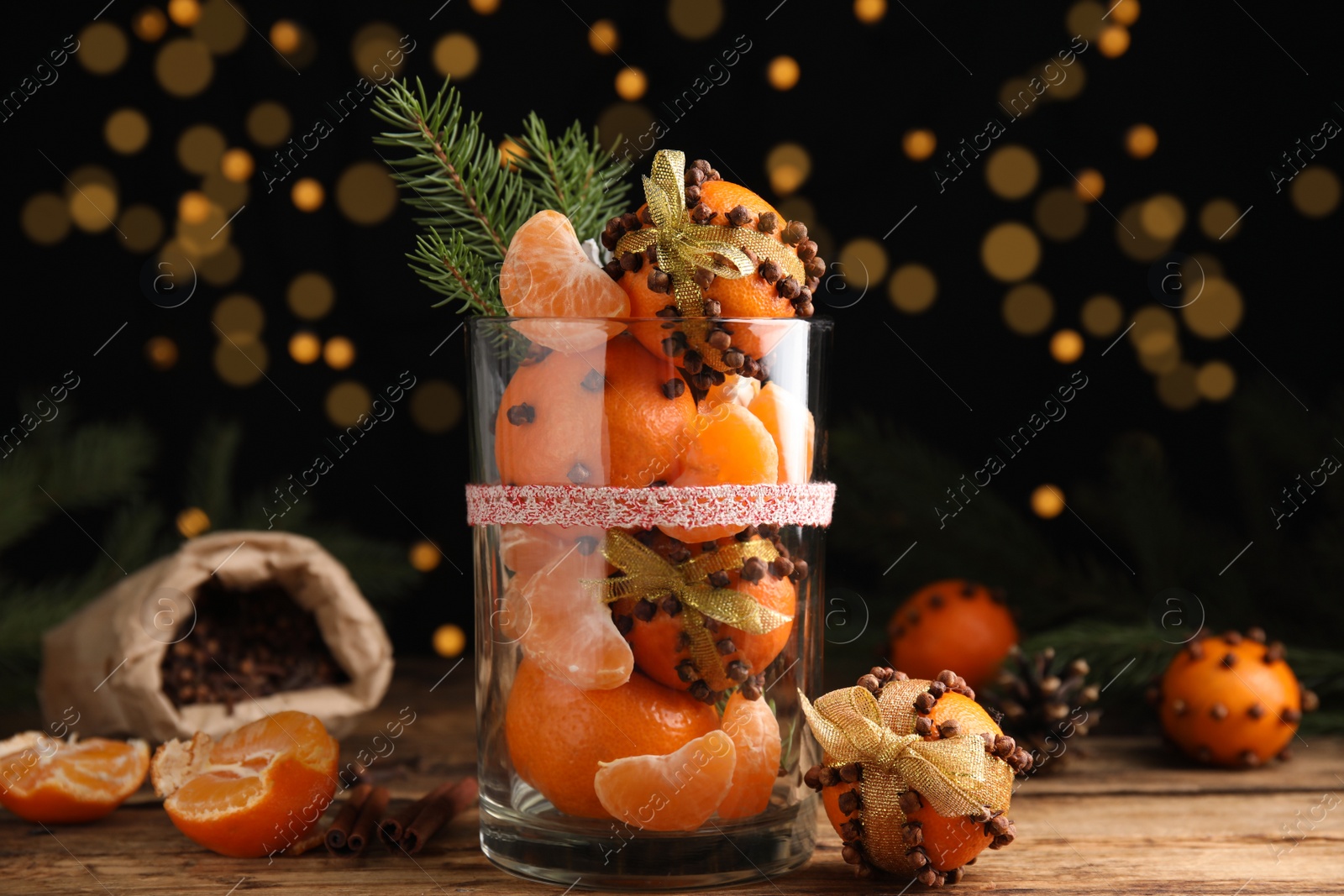 Photo of Christmas composition with tangerine pomander balls in glass against blurred lights