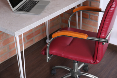 Comfortable red desk chair near table with laptop in modern office