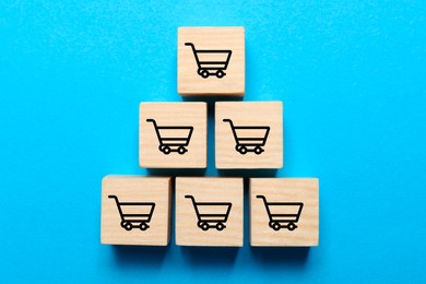 Wooden cubes with icons of shopping cart on light blue background, top view