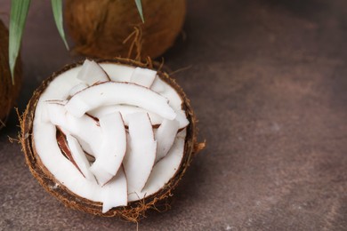 Coconut pieces in nut shell on brown table, space for text