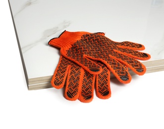 Stack of ceramic tiles and gloves on white background