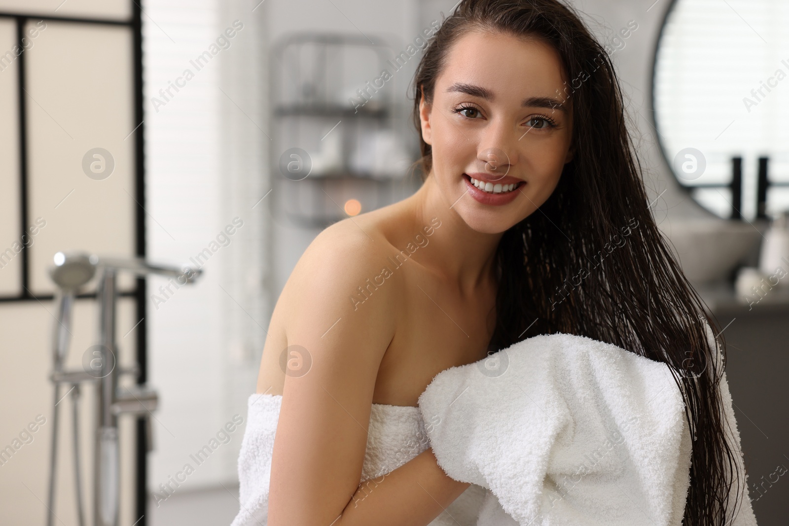 Photo of Smiling woman drying hair with towel after shower in bathroom