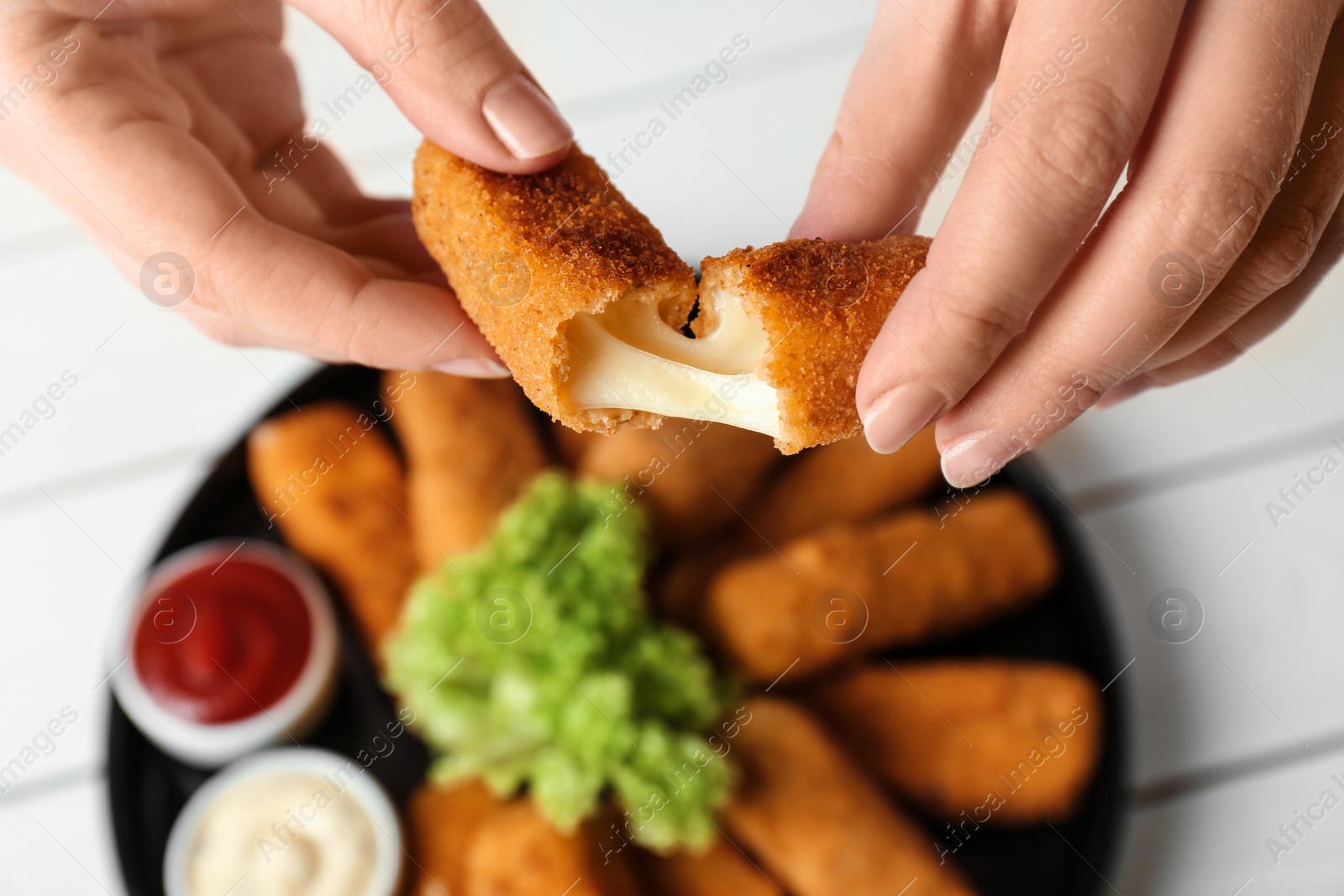 Photo of Woman holding broken cheese stick over plate, top view