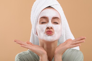 Photo of Woman with face mask sending air kiss on beige background. Spa treatments