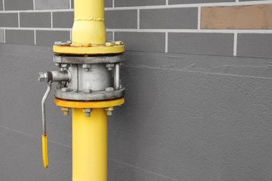 Photo of Yellow gas pipe with valve near brown wall outdoors, space for text
