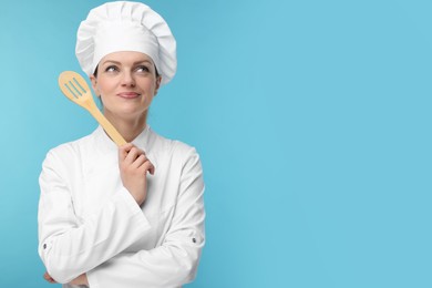 Photo of Happy chef in uniform holding wooden spatula on light blue background, space for text