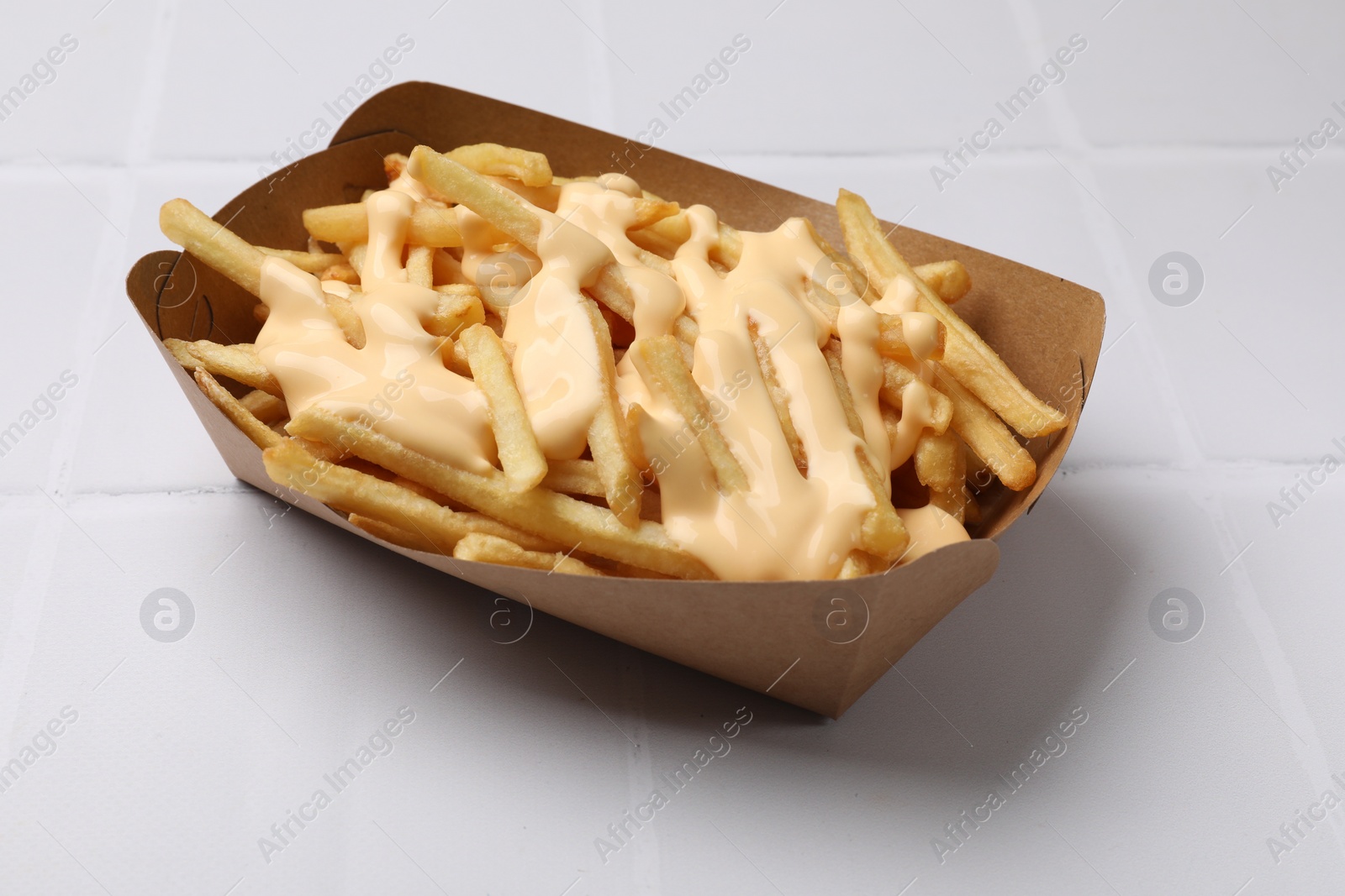 Photo of Delicious French fries with cheese sauce on white tiled table, closeup