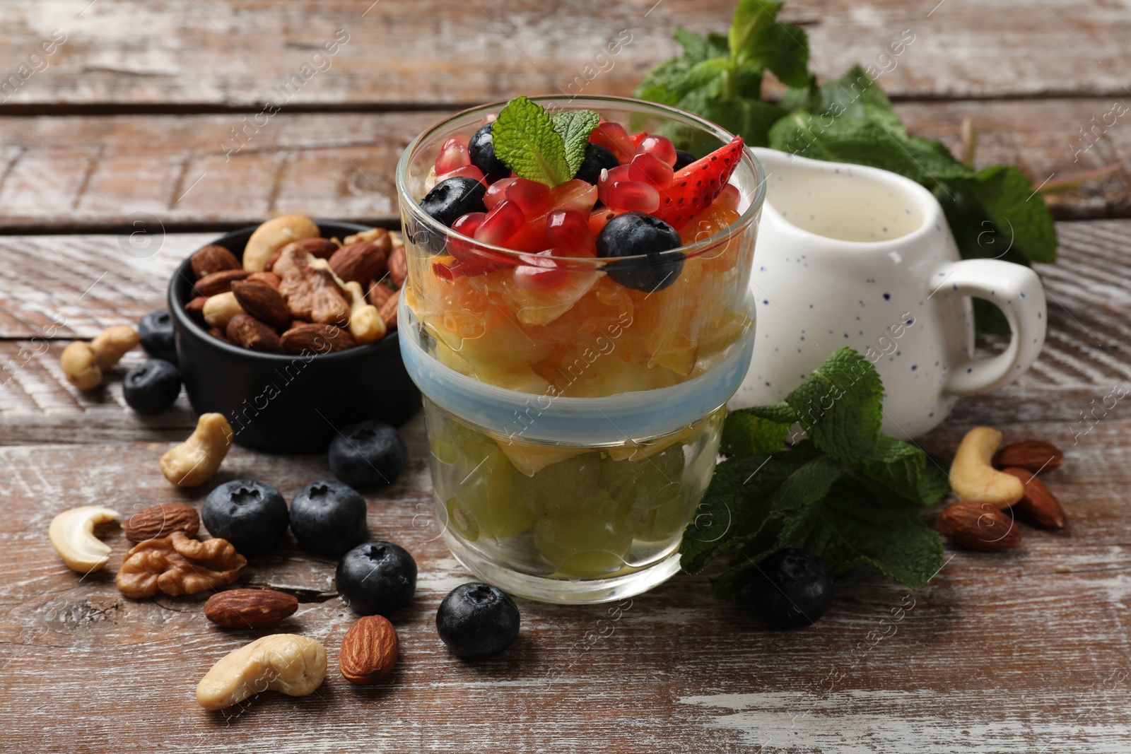 Photo of Delicious fruit salad, fresh berries, mint and nuts on wooden table