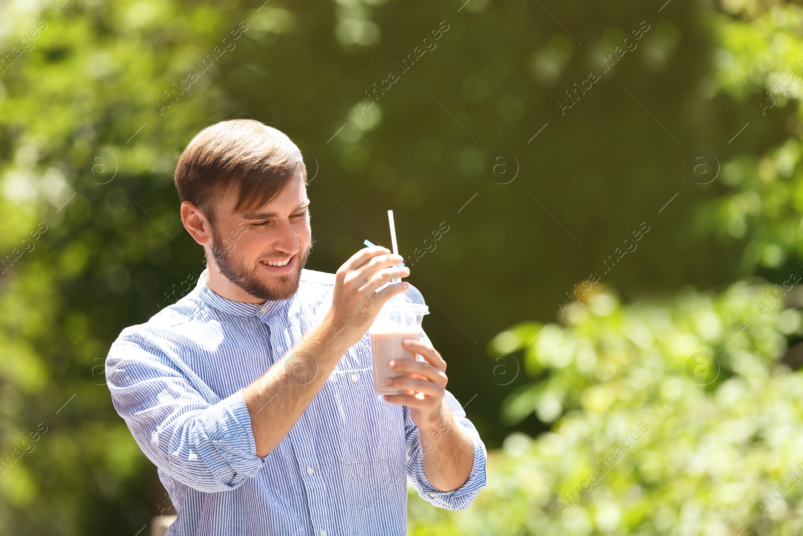 Photo of Young man with cup of delicious milk shake outdoors