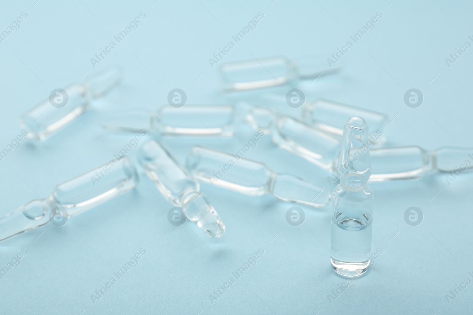 Photo of Glass ampoules with liquid on light blue background, closeup